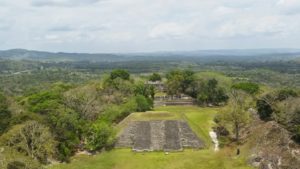 Aerial view of ancient ruins surrounded by lush greenery and distant hills.